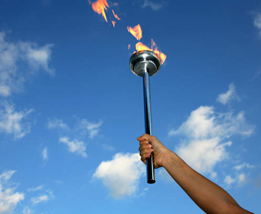 silhouetted hand holding burning flaming torch over cloudy sky.